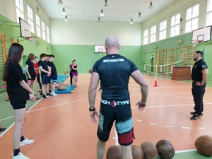 na sali gimnastycznej tyłem stoi instruktor, po prawej stronie stoi drugi instruktor, po lewej stronie stoją słuchacze