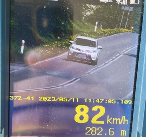 zdjęcie z fotoradaru, na dole napisana prędkość 82 km/h a na wyświetlaczu widać jadący ulicą biały samochód osobowy