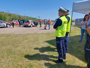 dwóch policjantów ruchu drogowego a przed nimi samochody rajdowe