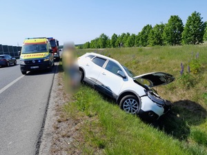 biały samochód osobowy w rowie, przy nim na drodze stoi karetka pogotowia