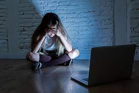 dziewczynka siedząca przy ścianie z pochyloną głową przed laptopem