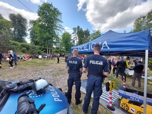 dwaj policjanci stojący tyłem, obok nich stoisko profilaktyczne policji