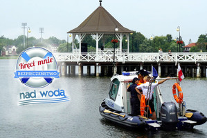 na jeziorze płynąca łódź policyjna, w tle widoczny pomost z wiatą, z lewej strony logo akcji Kręci mnie bezpieczeństwo nad wodą