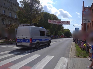 Przejeżdżający radiowóz policyjny po bokach na chodnikach podczas parady pojazdów stoją ludzie