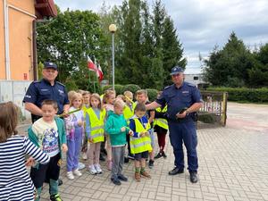 dwóch policjantów stojących przy gromadce dzieci. Osoby stoją na terenie zewnętrznym