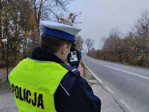 policjant ruchu drogowego mierzący prędkość przejeżdżających pojazdów miernikiem laserowym