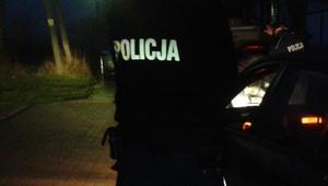policjant stojący nocą przy radiowozie