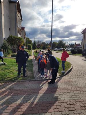 policjanci pokazują dzieciom, które stoją przed przejściem dla pieszych w jaki sposób należy przechodzić przez przejście dla pieszych