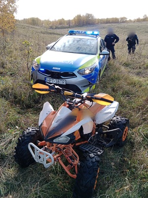 quad stojący przy radiowozie, za radiowozem stoi dwóch policjantów