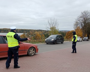 policjanci ruchu drogowego kierujący ruchem, obok nich przejeżdżające samochody