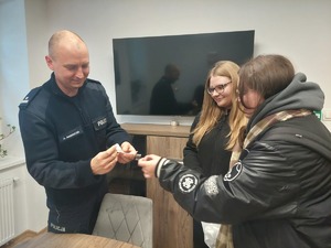 Policjant w gabinecie przyjmuje od dwóch kobiet białą wstążkę