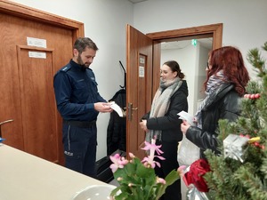 Policjant w gabinecie przyjmuje od dwóch kobieta białą wstążkę i ulotkę