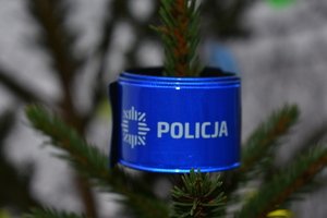 zawinięta opaska odblaskowa koloru niebieskiego z napisem Policja wokół gałązki choinki