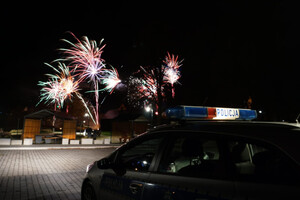 nocą na niebie fajerwerki a na pierwszym planie stoi radiowóz policyjny