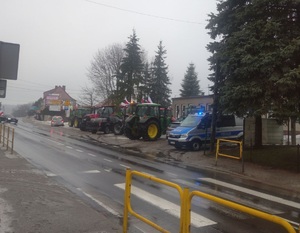 przy drodze stoi radiowóz policyjny a przy nim na poboczu ciągniki rolnicze