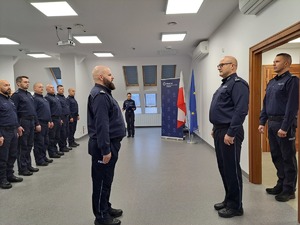 Na sali odpraw stoją policjanci, przed Komendantem Wojewódzkim Policji w Olsztynie stoi dowódca uroczystości i składa meldunek