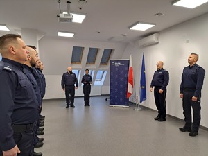 Na sali odpraw stoją policjanci przed Komendantem Wojewódzkim Policji w Olsztynie i p.o. Komendanta Powiatowego Policji w Mrągowie