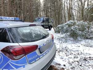 w lesie zimą swoi radiowóz policyjny a w tle wóz patrolu saperskiego