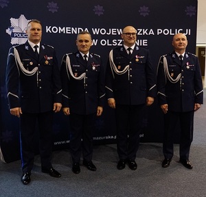 na sali stoi czterech policjantów w umundurowaniu galowym. Drugi z prawej strony stoi Komendant Wojewódzki Policji w Olsztynie mł.insp. Paweł Krauz