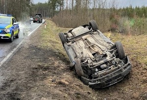 w przydrożnym rowie leży przewrócony na dach samochód osobowy. Na ulicy stoi radiowóz