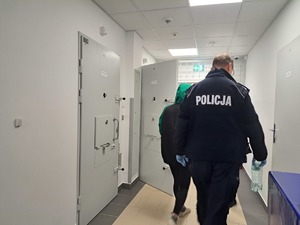 policjant idzie przez korytarz, przed nim idzie kobieta