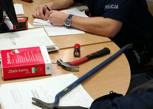 kodeks karny, młotek, łom leżący na stole, w tle widać siedzącego policjanta