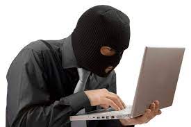 mężczyzna w koszuli z krawatem, ma na głowie założoną kominiarkę i pisze coś na laptopie