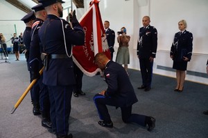 Nowy Komendant Wojewódzki Policji w Olsztynie insp. Mirosław Elszkowski klęka przed sztandarem KWP w Olsztynie. Sztandar trzymają policjanci