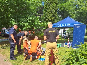 na pikniku profilaktycznym stoją policjanci, strażacy oraz klęczą ratownicy medyczni