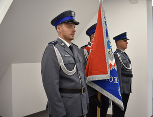 stojący na sali odpraw policjanci w poczcie swztandarowym ze sztandarem