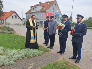 policjanci i ksiądz stoją przy obelisku Marka Cekały. Policjanci trzymają znicz i kwiaty