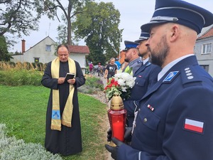 policjanci i ksiądz stoją przy obelisku Marka Cekały. Policjanci trzymają znicz i kwiaty