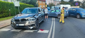 stojące na drodze rozbite samochody a obok nich strażacy i policjanci