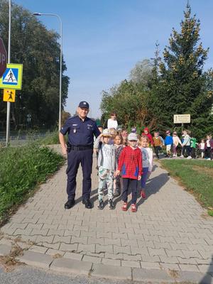 Policjant stoi z dziećmi przy znaku przejście dla pieszych