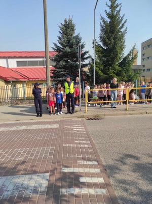 policjant i policjantka stoją z dziećmi przed przejściem dla pieszych