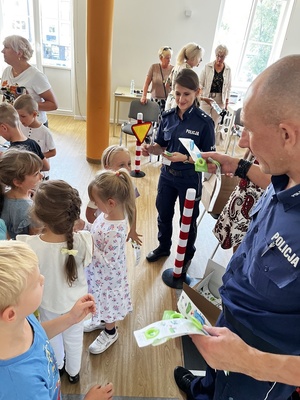 policjant i policjantka rozdają stojącym przed nimi dzieciom opaski