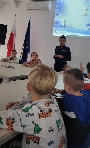 dzieci siedzące przy stole na sali odpraw a przed nimi policjantka