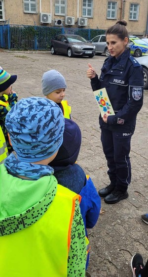 stojąca przed dziećmi policjantka, która pokazuje palcem symbol ok