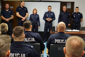 policjanci siedzący na sali i stojący przed nimi policjanci kadry kierowniczej z Komendantem Wojewódzkim Policji w Olsztynie na czele