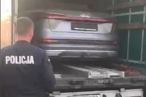 policjant stojący przy naczepie samochodu  ciężarowego na której widać pojazd audi