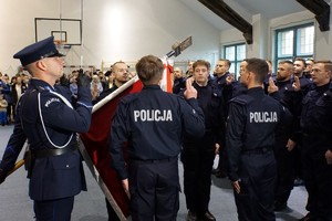 na sali stojący policjant ze sztandarem i nowo przyjęci policjanci składający ślubowanie