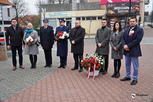 I Zastępca Komendanta Powiatowego Policji w Mrągowie kom. Michał Szynaka oraz Zastępca Komendanta Powiatowego Państwowej Straży Pożarnej w Mrągowie oraz przedstawiciele lokalnych samorządów stoją z kwiatami