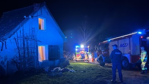 nocą policjant stoi przy budynku, obok niego stoi wóz strażacki