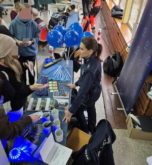 stoisko profilaktyczne promujące zawód policjanta i stojąca przy nim policjantka