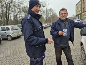 policjant i mężczyzna trzymający w ręku serduszko- zawieszki do samochodu z napisami przypominającymi kierującym o zachowaniu ostrożności przy zbliżaniu się do przejść dla pieszych