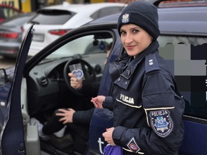 policjantka wręcza kierowcy siedzącemu w samochodzie serduszko- zawieszkę do samochodu z napisami przypominającymi kierującym o zachowaniu ostrożności przy zbliżaniu się do przejść dla pieszych