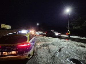 z lewej strony stoi radiowóz a na drodze policjant zatrzymuje pojazd do kontroli trzeźwości