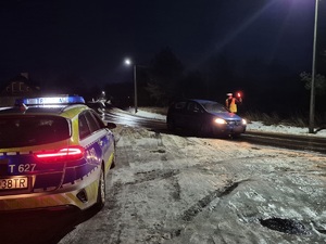 z lewej strony stoi radiowóz a na drodze policjant zatrzymuje pojazd do kontroli trzeźwości