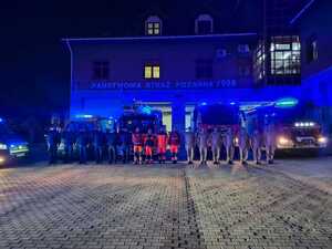 stojący na placu policjanci, ratownicy medyczni, strażacy oraz ich pojazdy służbowe z włączonymi sygnałami świetlno dźwiękowymi. Policjanci, ratownicy medyczni, strażacy oddają honor