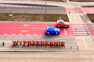 jadące ulicą dwa samochody koloru niebieskiego i czerwonego zbliżające się do przejścia dla pieszych